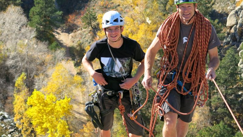 Two climbers rope up together. One climber is looking at the camera and smiling.