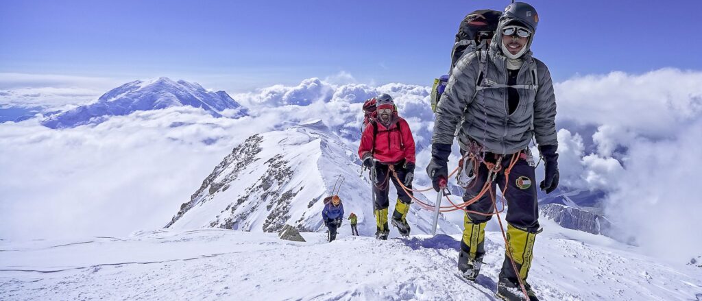 Three climbers ascend a snowy path in a remote mountain range covered in snow.