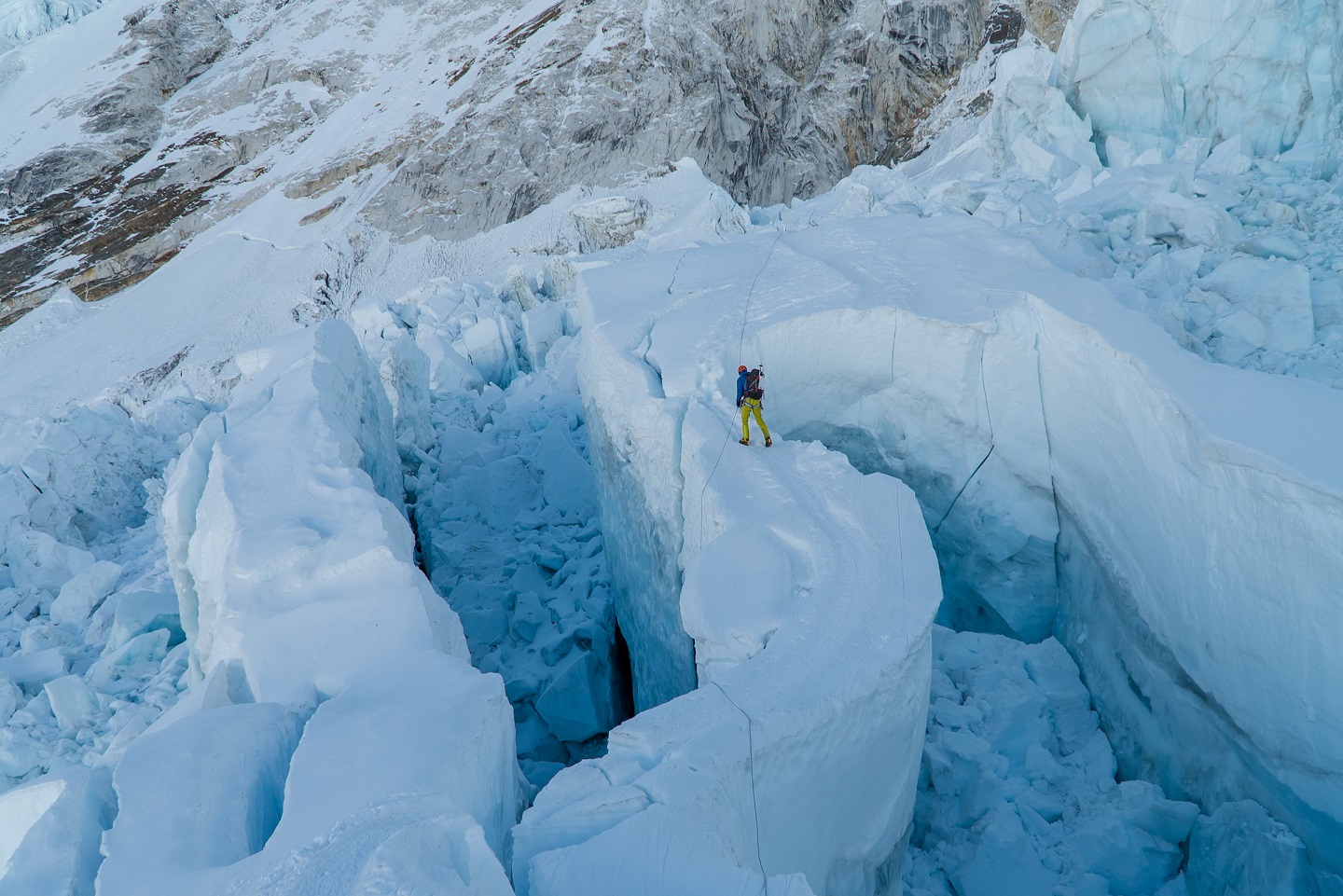 A top down view of a climber traversing narrow glaciated terrain. The climber is using ropes to safely navigate large crevasses.