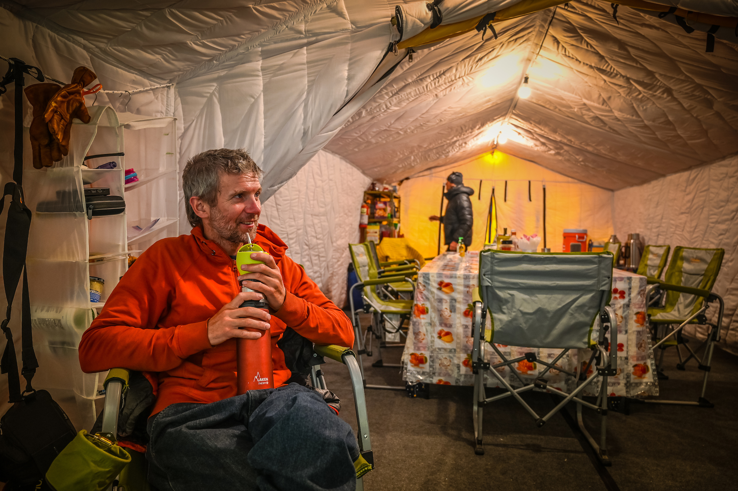 A man in a red top sits in a comfortable expedition tent. 
