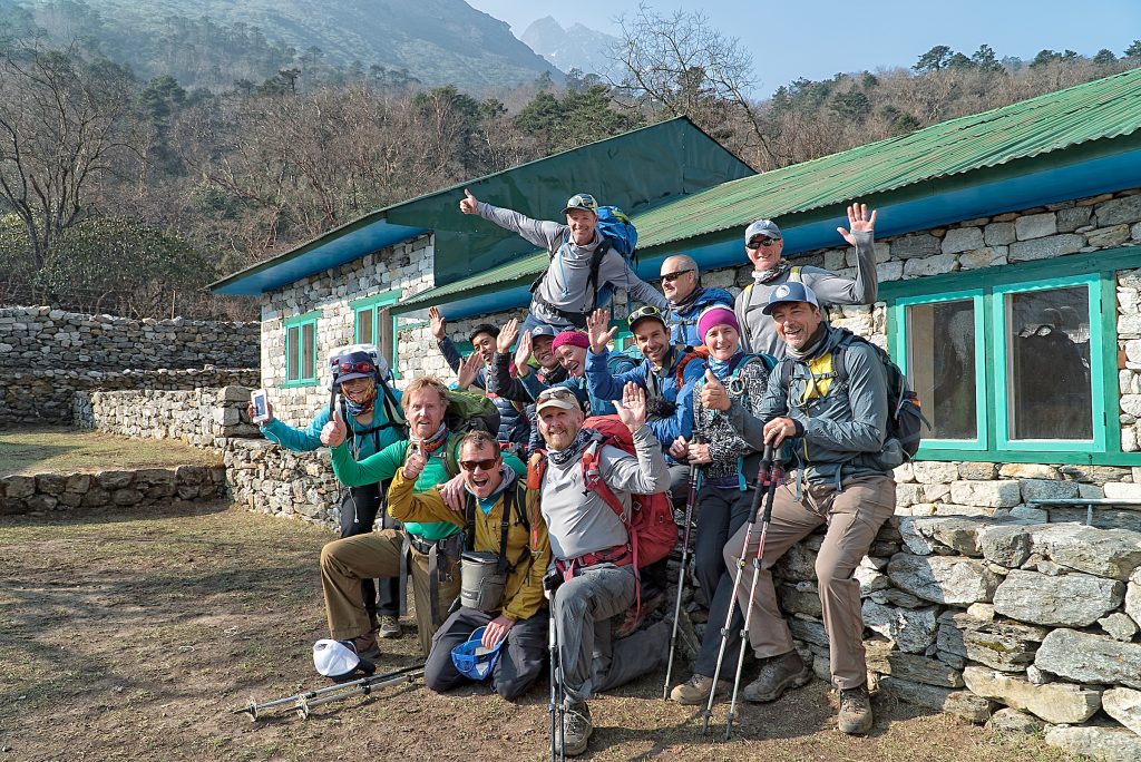 A group of Everest base camp trekkers sitting on a stone wall posing for a photo, all smiling.